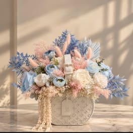 Pastel blue and cream floral arrangement in a white monogram handbag-style vase