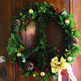 Christmas wreath with pinecones, red berries, and a gold bow on a wooden door