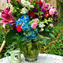 Colorful mixed bouquet in a glass vase with a mug beside it