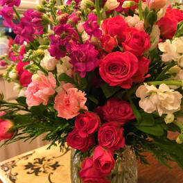 Bouquet of pink roses, carnations, and purple blooms in a glass vase