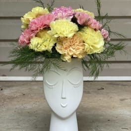 Pastel carnations arranged in a white face-shaped vase