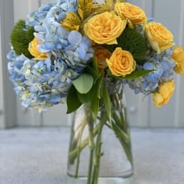 Blue hydrangeas and yellow roses arranged in a clear glass vase