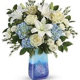 White lilies and roses with blue hydrangeas in a blue glass vase