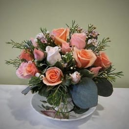Pink and peach roses arranged in a low white bowl
