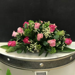 Low arrangement of light and hot pink roses with white filler flowers in a silver container