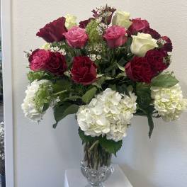 Tall glass vase with white hydrangeas and red, pink, and cream roses in a mixed arrangement