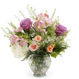 Mixed bouquet of purple roses, peach spray roses and white hydrangeas in a clear glass vase