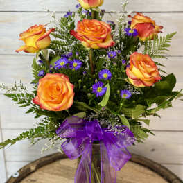 Bouquet of orange-yellow roses with purple daisies in a glass vase
