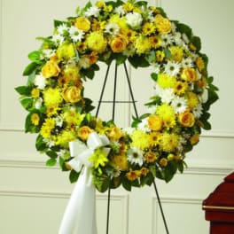 Yellow and white floral wreath on a black easel with a white ribbon