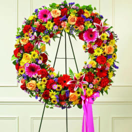 Large colorful floral wreath on a black easel with a pink ribbon