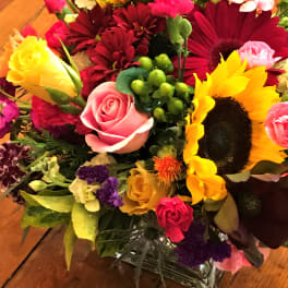 Mixed bouquet with sunflowers, roses, and gerbera daisies in a glass vase