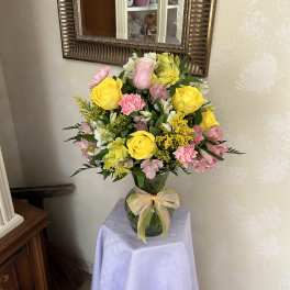 Mixed bouquet of yellow roses, pink carnations, and white flowers in a glass vase
