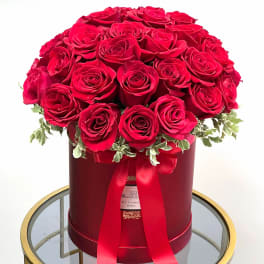 Red roses arranged in a round hat box with a ribbon