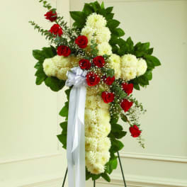 Standing floral cross with white flowers, red roses, and a white ribbon