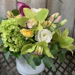 Bouquet of green orchids, hydrangea, roses, and calla lilies in a white vase