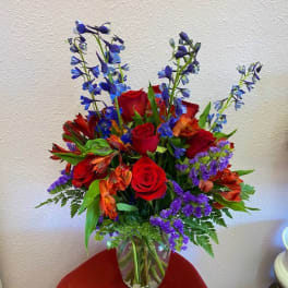 Bouquet of red roses, orange flowers, and blue delphinium in a glass vase