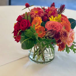 Mixed bouquet of red, orange, and pink flowers in a clear glass vase