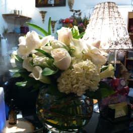 White floral arrangement in a round glass vase with calla lilies and roses