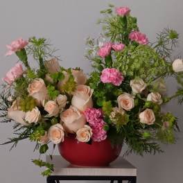 Pink and peach roses with carnations in a red vase