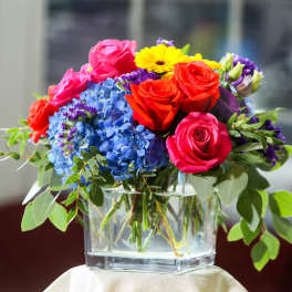 Colorful bouquet of roses, hydrangeas, and a yellow daisy in a glass vase