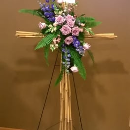 Standing floral cross with pink roses and purple flowers on a bamboo easel