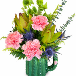 Pink carnations and blue thistles arranged in a green ceramic mug