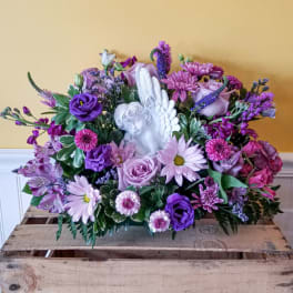 Purple and pink floral arrangement with a white angel figurine