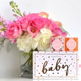 Pink roses and white hydrangeas in a glass vase with baby gift boxes