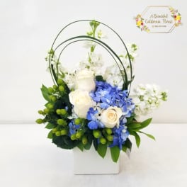 White and blue floral arrangement in a white box with arched handles