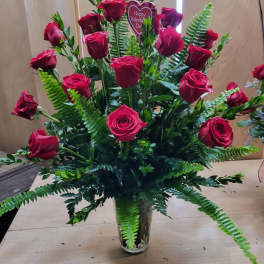 Tall bouquet of red roses in a clear glass vase with fern foliage