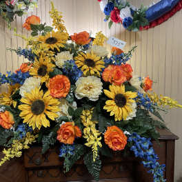 Large floral arrangement with sunflowers, orange roses, and blue flowers