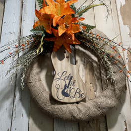 Orange lilies on a burlap wreath with a wooden guitar sign