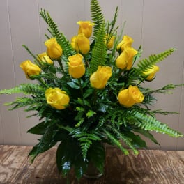 Yellow roses arranged in a glass vase with fern foliage