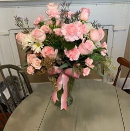 Pink roses and carnations in a glass vase with a pink ribbon