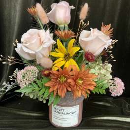 Mixed floral arrangement in a pink candle jar with pale roses and orange daisies