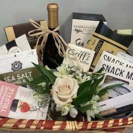 Gift basket with a small rose arrangement and assorted snacks, wine, and chocolates