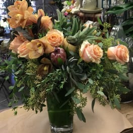 Peach roses and orchids in a glass vase with lush greenery