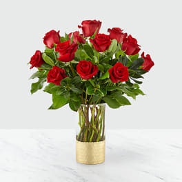 Red roses arranged in a clear glass vase with a gold wrap