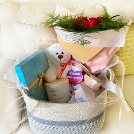 Gift basket with red roses, a teddy bear, chocolates, and a candle