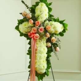 Cross-shaped floral spray with white blooms, peach roses, and a pink ribbon