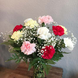 Mixed red, pink, white, and yellow carnations with baby's breath in a clear glass vase