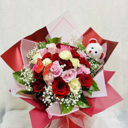 Bouquet of red, pink, and white roses with a small teddy bear