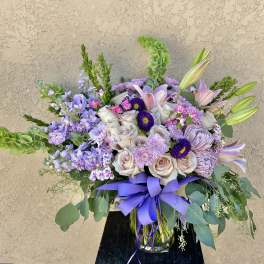 Lavender and blush mixed bouquet in a glass vase with a purple ribbon