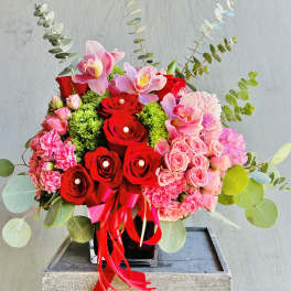 Red and pink floral arrangement in a black vase with ribbon