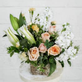 Peach roses and white lilies in a rustic container