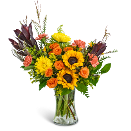 Bouquet of sunflowers, orange roses, and pink carnations in a glass vase