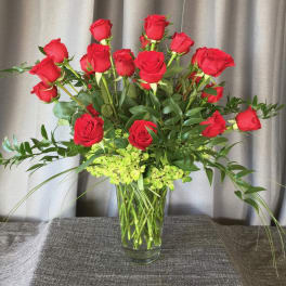 Red roses arranged in a clear glass vase with green filler