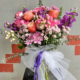 Pink and purple mixed bouquet in a glass vase with a white tulle bow