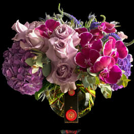 Bouquet of lavender roses, purple hydrangeas, and magenta orchids in a glass vase