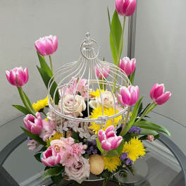 Pink tulips and mixed flowers arranged in a white birdcage centerpiece